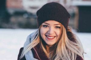 A young woman wearing a warm coat and hat smiles outside during the winter