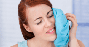 Woman holding a blue ice pack on her jaw after wisdom teeth removal.